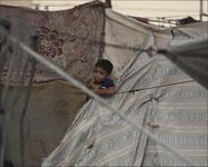 A little boy pokes his head, arms, and shoulders through hanging sheets and blankets
