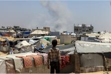 A Palestinian child looked on from his tent encampment as smoke billowed from buildings in the distance