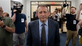 New York City Comptroller and mayoral candidate Brad Lander, wearing a blue suit, walks through a building while followed by photographers.