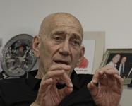 Ehud Olmert wearing a black dress shirt while speaking and gesturing with both hands touching his index and thumb fingers together