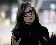 Francesca Albanese wearing a black top with black rimmed glasses and gesturing with both hands open with her palms facing toward her audience