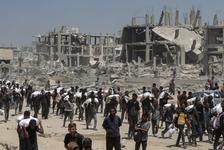Hundreds of Palestinians carry white sacks of flour on their shoulders as they walk past destroyed structures