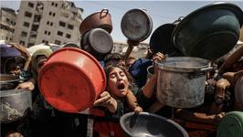 A crowd of people pile together holding out containers to collect food