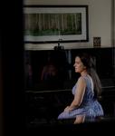 Ms. Rachel wearing a blue and white striped sleeveless dress seated in front of a black upright piano