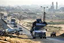 Vehicles move past destroyed buildings along a paved road