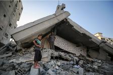 A Palestinian boy and a man stand amid the destruction of a building