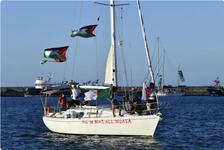 Activists taking part in the Global Sumud Flotilla stand on the deck displaying Palestinian flags and writing on the side that reads, "All in boat, all in Gaza"