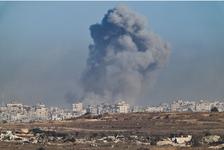 A massive, dark gray plume of smoke rises over damaged buildings