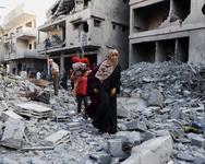 A woman leads children over the rubble of destroyed buildings.