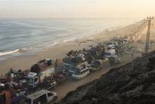 A long line of vehicles moves along the coast. Some have piles of belongings stacked on car roofs.