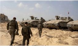 Three IDF soldiers walk toward three tanks parked on the sand
