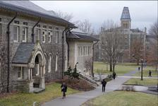 Students walking past gray brick buildings at Cornell University on a cloudy day