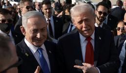 Netanyahu and Trump stand next to each other surrounded by a group of people as they smile and Trump points toward him