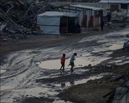Two children play near large puddles in front of makeshift tents