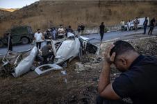 People inspect the remains of a heavily damaged vehicle on the side of a road