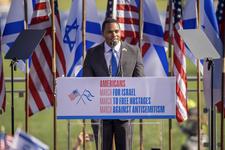 Ritchie Torres speaks during March For Israel. He is standing at a lectern on a stage in front of a row of American and Israeli flags.