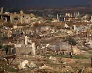 An adult and two children move through the ruins of destroyed homes and buildings