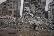 A Palestinian man rides a bicycle past destroyed buildings