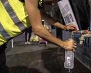 A person in a neon vest fills a bottle with water from an emergency tank