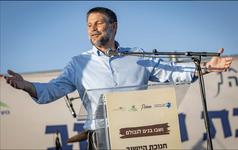 Finance Minister Bezalel Smotrich stands at a lectern with his arms outstretched
