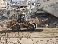 A child watches a bulldozer move across a dirt path past heaping piles of rubble and debris