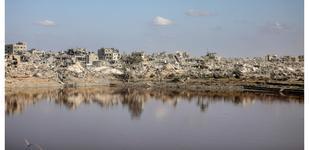 A body of water sits in front of a landscape of heavily damaged buildings