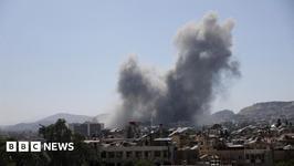 Multiple plumes of gray smoke rise from city buildings and fill the air