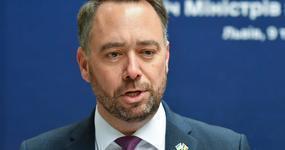 Belgian Foreign Minister Maxime Prévot wearing a dark suit with white dress shirt and purple necktie speaks in front of a blue background